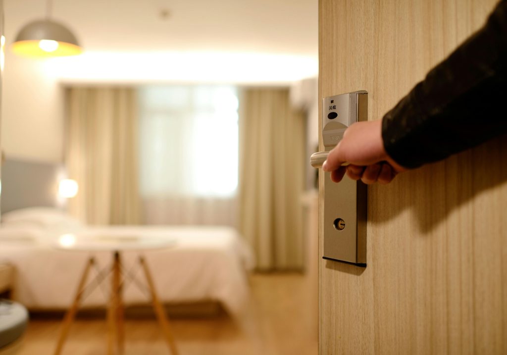 A person opening a hotel room door to view an emtpy room