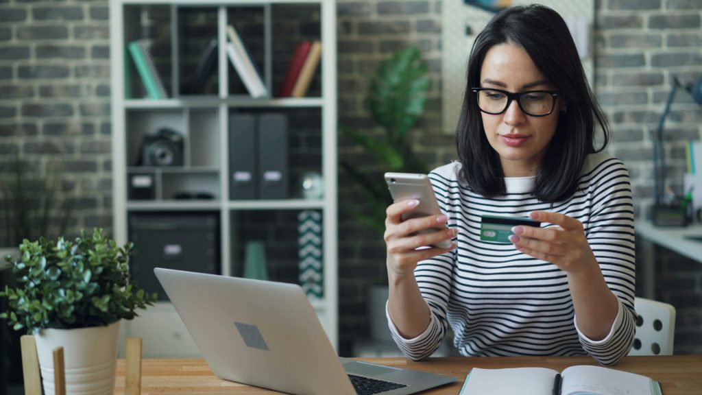 Woman entering credit card to pay for an online transaction with computer in front of her